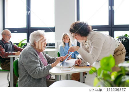 Teacher helping old woman to learn digital skills. 136336877