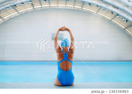 Rear view of female swimmer stretching before swim in pool. 136336963