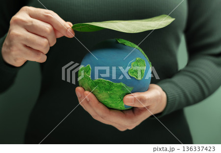 Hands holding globe with green leaf symbolizing environmental protection, sustainability 136337423