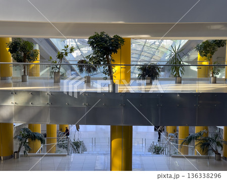 Spacious interior of a modern public building with indoor plants arranged along glass railings and 136338296