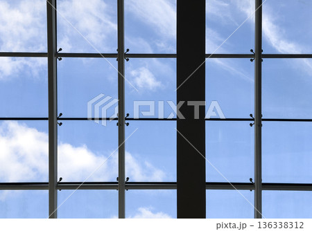 Upward view of a modern glass roof with metal framing against a blue sky with soft clouds. Clean Upward view of a modern glass roof with metal framing against a blue sky with soft clouds. Clean 136338312