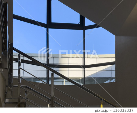 Interior view of a modern building with a staircase and large panoramic windows against a clear blue Interior view of a modern building with a staircase and large panoramic windows against a clear blue 136338337