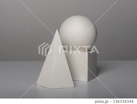 Minimal still life with white geometric solids including a pyramid, cube, and sphere stacked in a 136338348