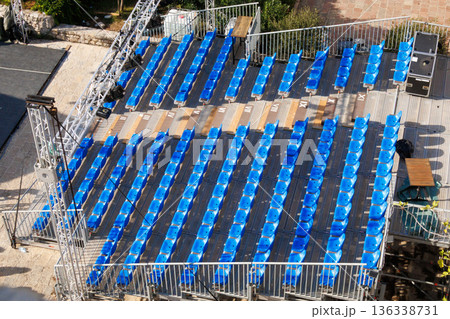 Empty outdoor stadium grandstand with blue plastic seats viewed from above. Sports venue infrastructure, sunny day, no spectators. Empty outdoor stadium grandstand with blue plastic seats viewed from above. Sports venue infrastructure, sunny day, no spectators. 136338731