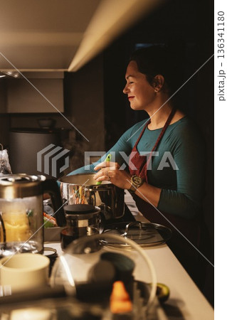 Woman Cooking in Kitchen with Joyful Expression 136341180