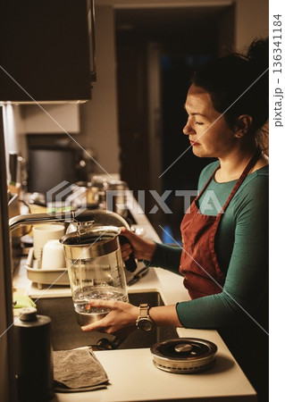 Woman Pouring Purified Water from Home Purifier 136341184