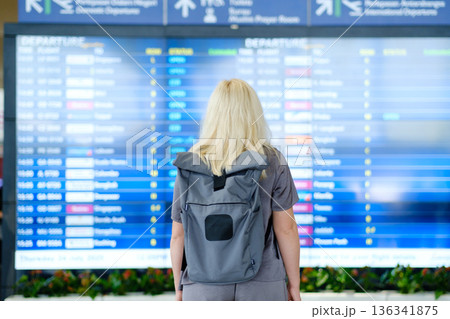 Traveling to new destinations as a woman checks the departure board at an airport, planning her next journey on a summer Thursday in July Traveling to new destinations as a woman checks the departure board at an airport, planning her next journey on a summer Thursday in July 136341875