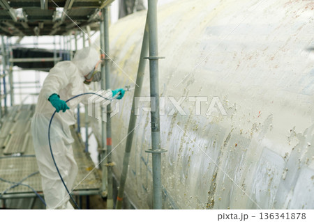 A worker in protective gear applies a coating to the aluminum surface of the aircraft to clean it from paint on a working day 136341878