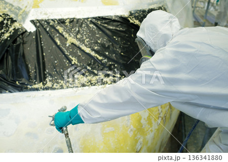 Professional worker applies spray paint to an aircraft in a hangar during repairs, ensuring precision and safety while wearing protective gear Professional worker applies spray paint to an aircraft in a hangar during repairs, ensuring precision and safety while wearing protective gear 136341880