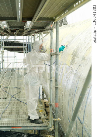 Worker in protective gear conducts maintenance on large industrial equipment at a construction site during daylight hours 136341883