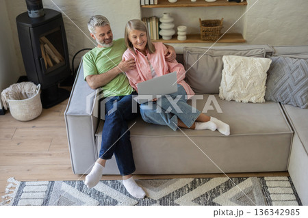 Older adults relaxing on couch looking at laptop screen 136342985