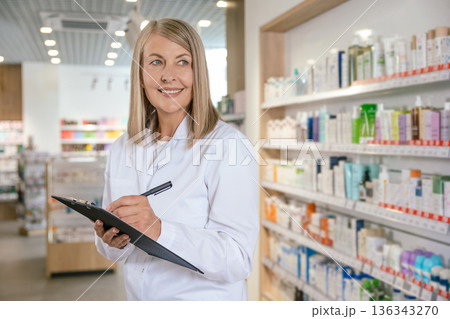 Mature blonde pharmacist in a lab coat in a drug store Mature blonde pharmacist in a lab coat in a drug store 136343270