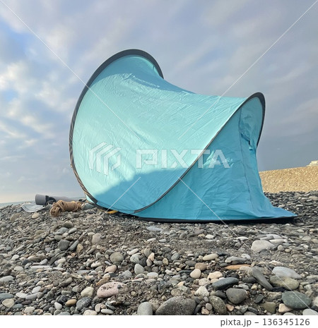 Tent set up on rocky beach with cloudy sky in the background during daytime near a coastal area 136345126