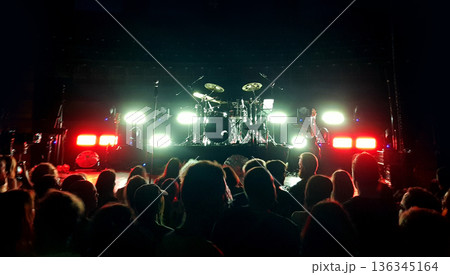 Crowd gathers for a live music performance in a venue with bright lights and a drum set on stage Crowd gathers for a live music performance in a venue with bright lights and a drum set on stage 136345164