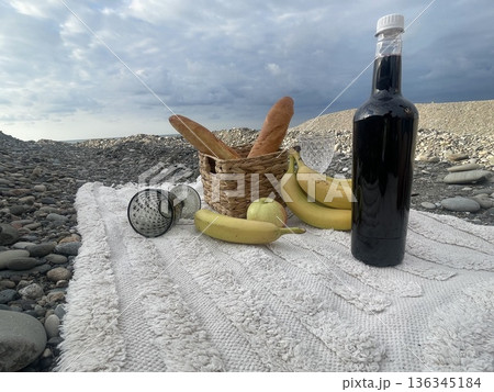 Empty beach scene with a picnic setup featuring bread, fruit, and a drink  136345184