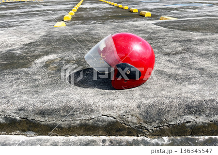 red open face motorcycle helmet on concrete pavement near row of yellow parking wheel stops 136345547
