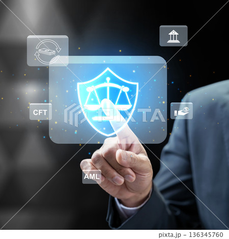 Businessman interacting with a futuristic digital interface for AML and CFT compliance, featuring a legal shield and scales representing financial security and regulatory law 136345760