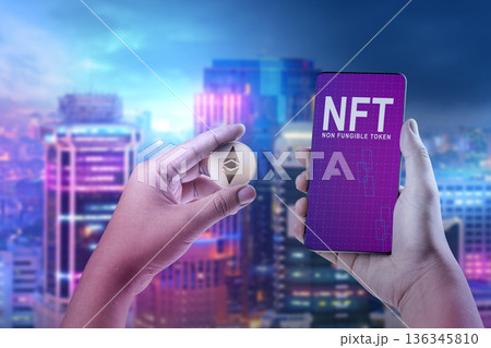 A person holding an Ethereum physical coin and a mobile phone displaying NFT text against a bokeh city night background. Concept of digital art and cryptocurrency A person holding an Ethereum physical coin and a mobile phone displaying NFT text against a bokeh city night background. Concept of digital art and cryptocurrency 136345810