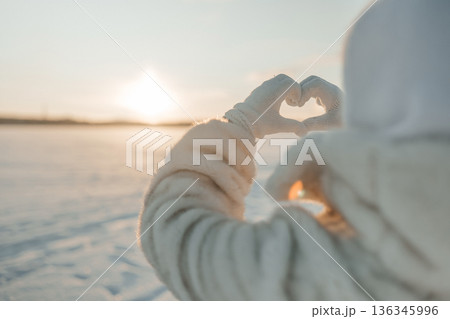 Making a heart shape with hands during sunset on a snowy landscape 136345996