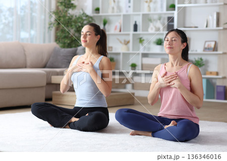 Two diverse friends at home doing yoga breathing exercises Two diverse friends at home doing yoga breathing exercises 136346016