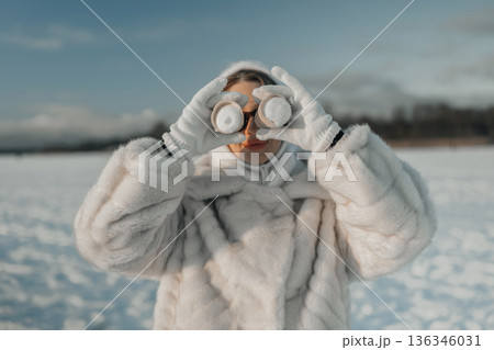 Person wearing a white coat looks through binoculars on a snowy field during daylight 136346031