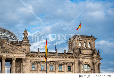 Berlin, germany, august 12, 2023. Reichstag building facade in berlin, germany. German flags waving from the historic parliament building under a blue sky with clouds Berlin, germany, august 12, 2023. Reichstag building facade in berlin, germany. German flags waving from the historic parliament building under a blue sky with clouds 136346066