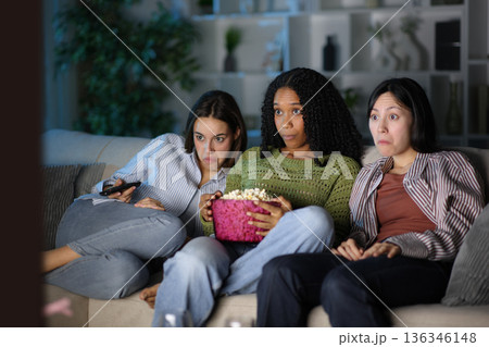Three diverse amazed friends watching tv in the night Three diverse amazed friends watching tv in the night 136346148