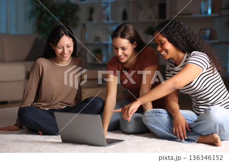 Three diverse friends checking laptop content in the night at home 136346152