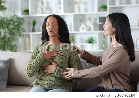 Woman teaching friend to do breathing exercises at home 136346194
