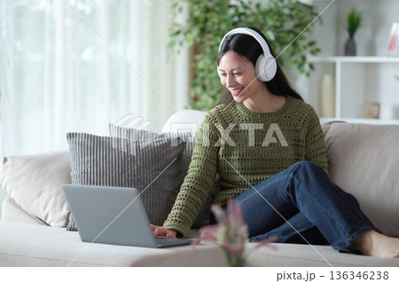 Asian woman watching media on personal computer on a couch Asian woman watching media on personal computer on a couch 136346238