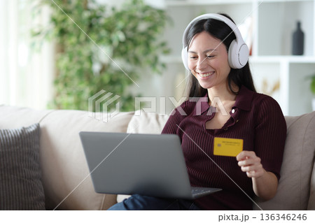 Happy asian woman buying online media at home Happy asian woman buying online media at home 136346246