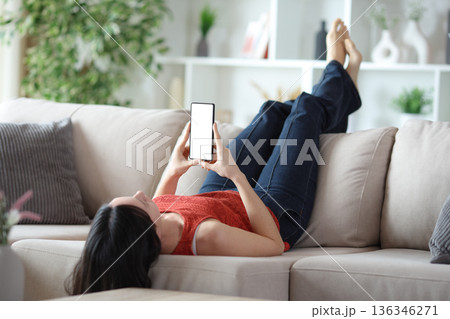 Woman lying on a couch using phone with blank screen 136346271