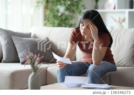 Worried asian woman checking bill on a sofa at home 136346273