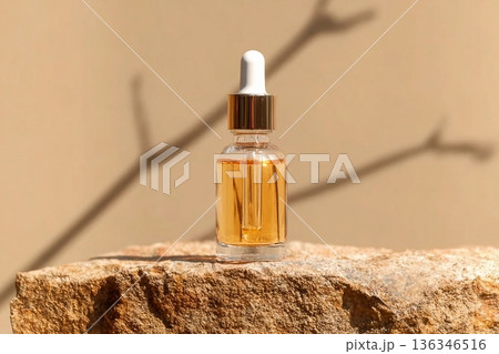A cosmetic packaging mockup showing a clear serum bottle resting on a rock, set against beige backdrop for a clean and elegant aesthetic. 136346516