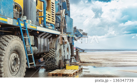 A drilling rig is positioned near the shoreline. Workers manage the rig as it extracts oil and gas resources. The weather shows cloudy skies and water nearby A drilling rig is positioned near the shoreline. Workers manage the rig as it extracts oil and gas resources. The weather shows cloudy skies and water nearby 136347739