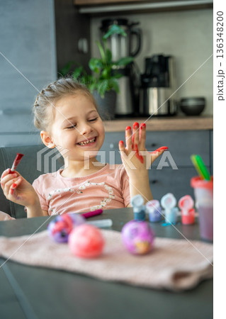Little girl painting her hand with red paint while decorating Easter eggs at home. Creative Easter activity, childhood curiosity and playful holiday preparation indoors. Little girl painting her hand with red paint while decorating Easter eggs at home. Creative Easter activity, childhood curiosity and playful holiday preparation indoors. 136348200