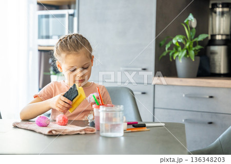 Little girl decorating Easter eggs with colorful stickers while sitting at table at home. Creative Easter activity, simple egg decoration technique and joyful holiday preparation indoors. Little girl decorating Easter eggs with colorful stickers while sitting at table at home. Creative Easter activity, simple egg decoration technique and joyful holiday preparation indoors. 136348203