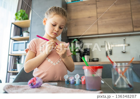 Child using both hands to steady egg while painting. Visual metaphor for balance, growth, and developing skills through craft. 136348207