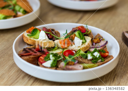 Close-up of a white plate with assorted gourmet canapes and mini sandwiches. 136348582