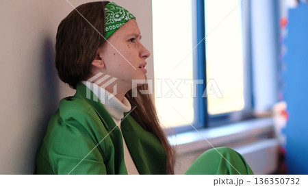 A girl in a vibrant green outfit curls into herself, her posture reflecting vulnerability and emotional contemplation. The soft lighting enhances the mood of solitude and inner reflection. A girl in a vibrant green outfit curls into herself, her posture reflecting vulnerability and emotional contemplation. The soft lighting enhances the mood of solitude and inner reflection. 136350732