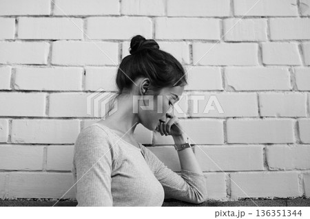 White Woman Seated Against Brick Wall, Pensive Writer Sketching Thoughts, Monochrome Mood, Soft Side Lighting, Textured Background, Casual Top And Bun, Intimate Contemplative Atmosphere, Urban Minimal 136351344