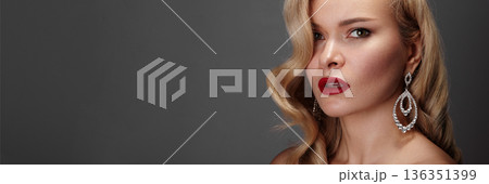Closeup Caucasian Woman Wearing Diamond Earrings, Red Lipstick, Wavy Blonde Hair, Gray Studio Background, Luxury Jewelry Campaign Mood, Poised Expression, Dramatic Side Lighting, High Fashion Styling 136351399