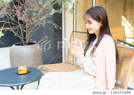 カフェのテラス席で紅茶を飲みながらスマホを使う女性 カフェのテラス席で紅茶を飲みながらスマホを使う女性 136351846