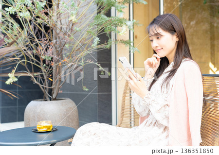 カフェのテラス席で紅茶を飲みながらスマホを使う女性 カフェのテラス席で紅茶を飲みながらスマホを使う女性 136351850