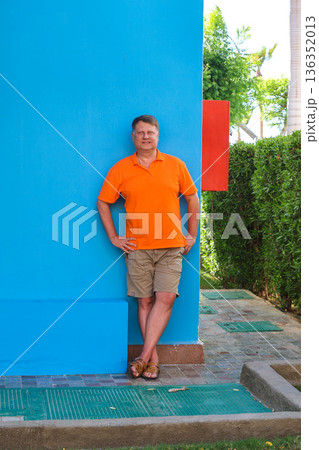 Portrait of an adult blond man against the blue wall of his house 136352013