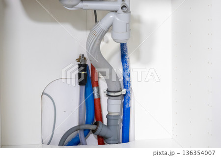 Detailed view of under sink plumbing, revealing a drain hose, red and blue water supply lines, essential for home renovation and repair projects 136354007