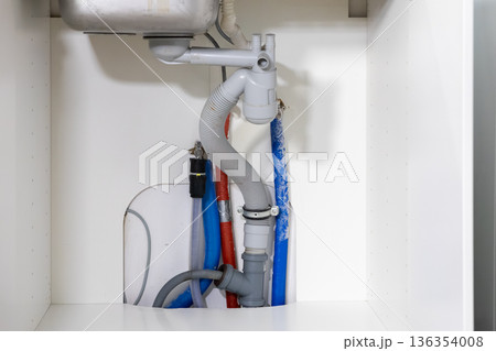 Modern kitchen sink plumbing system with exposed grey drainage pipes and colorful water supply lines, illustrating essential home utility piping and maintenance Modern kitchen sink plumbing system with exposed grey drainage pipes and colorful water supply lines, illustrating essential home utility piping and maintenance 136354008