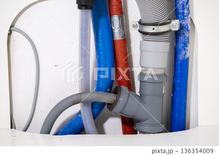 Arrangement of plumbing pipes, flexible hoses, and cables in a wall cavity, representing essential household utility infrastructure for home installation and repair 136354009