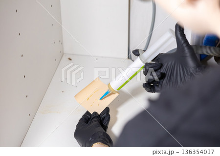 Gloved professional hand applying cockroach pest control gel bait inside a dirty kitchen cabinet, depicting effective extermination and home hygiene management 136354017