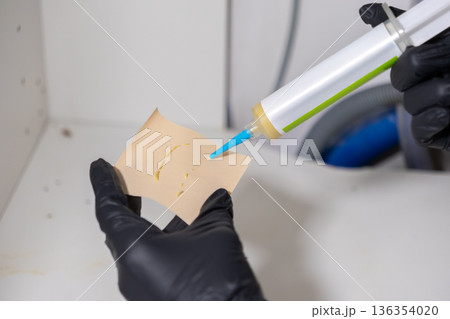 Person wearing black protective glove applying insecticidal gel from a tube onto paper for effective pest control or professional home extermination service 136354020